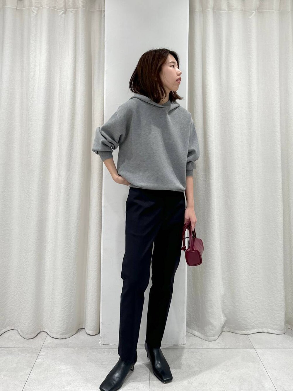 レッド系のショルダーバッグ、ブラック系のスラックス、グレー系のパーカーを着用したレディースの秋コーディネートの3枚目の写真