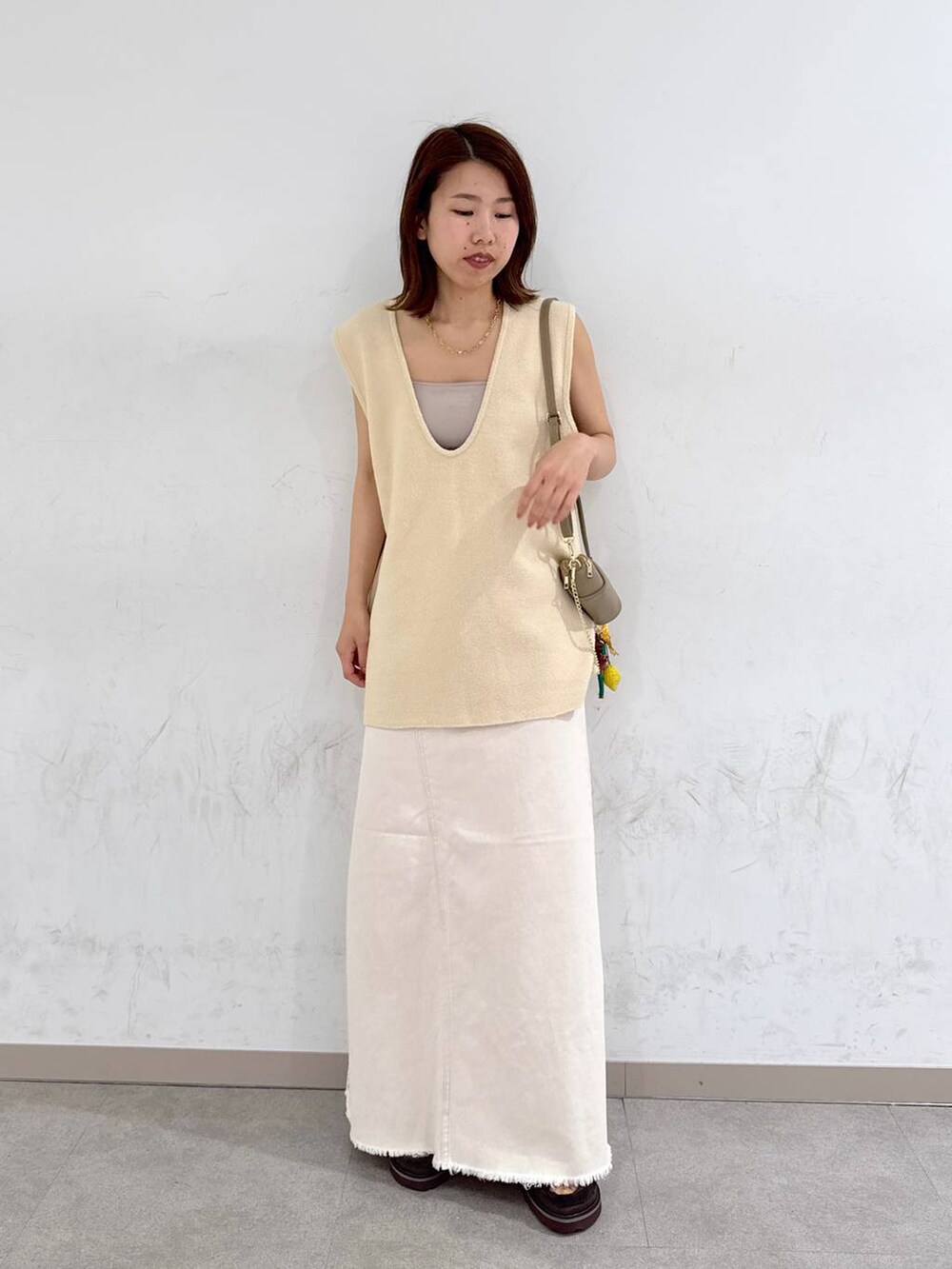 オレンジ系のキャミソール、ホワイト系のスカート、ベージュ系のベストを着用したレディースの夏コーディネートの2枚目の写真