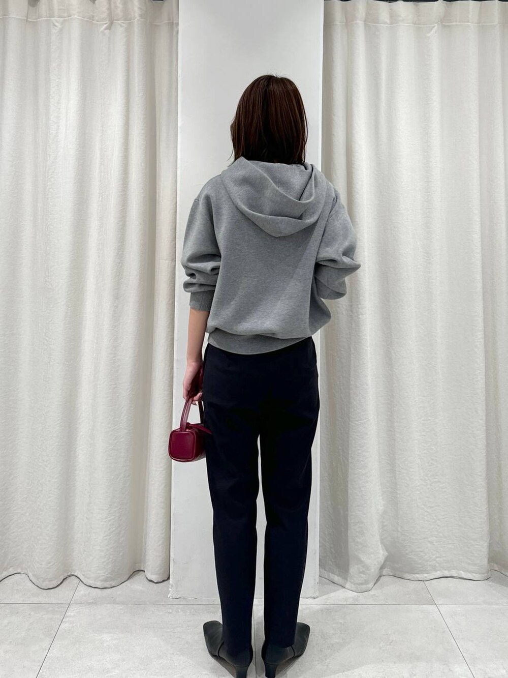 レッド系のショルダーバッグ、ブラック系のスラックス、グレー系のパーカーを着用したレディースの秋コーディネートの6枚目の写真