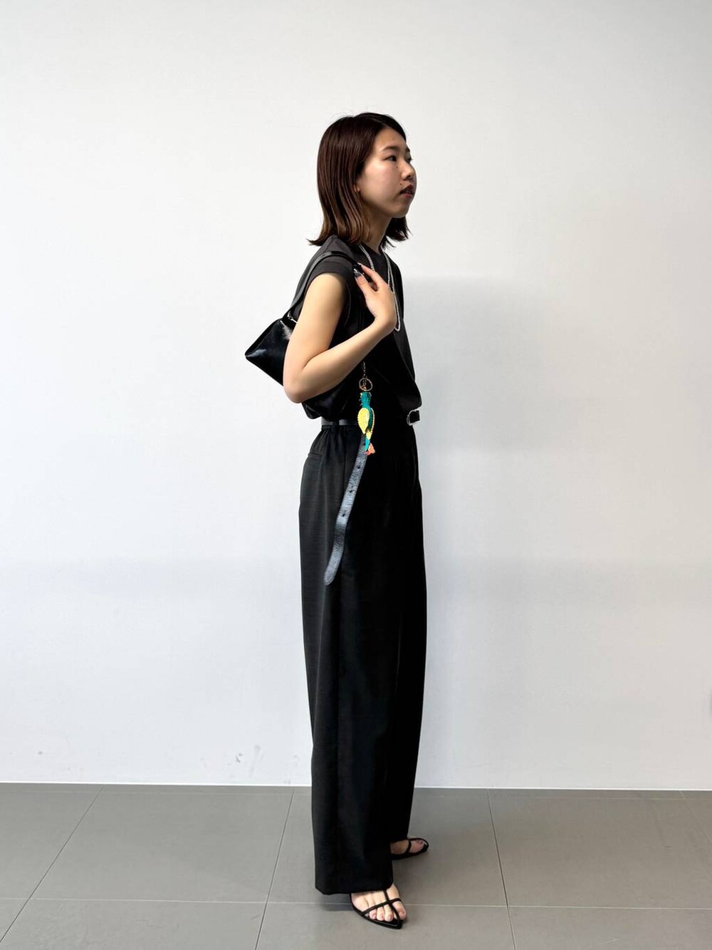 グレー系のタンクトップ、グレー系のスラックス、ブラック系のショルダーバッグを着用したレディースの夏コーディネートの4枚目の写真