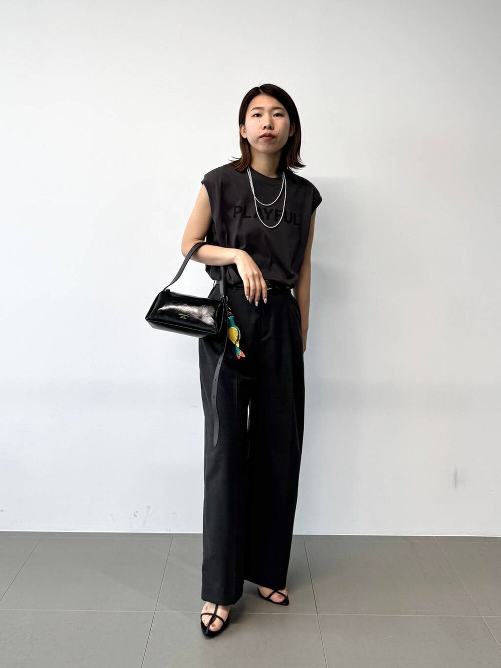 グレー系のタンクトップ、グレー系のスラックス、ブラック系のショルダーバッグを着用したレディースの夏コーディネートの6枚目の写真