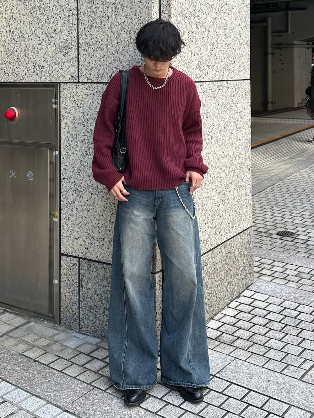 レッド系のニット/セーター、ブラック系のショルダーバッグ、ブルー系のデニムパンツを着用したメンズの秋コーディネートの3枚目の写真