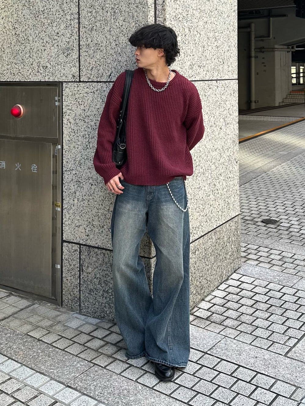 レッド系のニット/セーター、ブラック系のショルダーバッグ、ブルー系のデニムパンツを着用したメンズの秋コーディネートの2枚目の写真