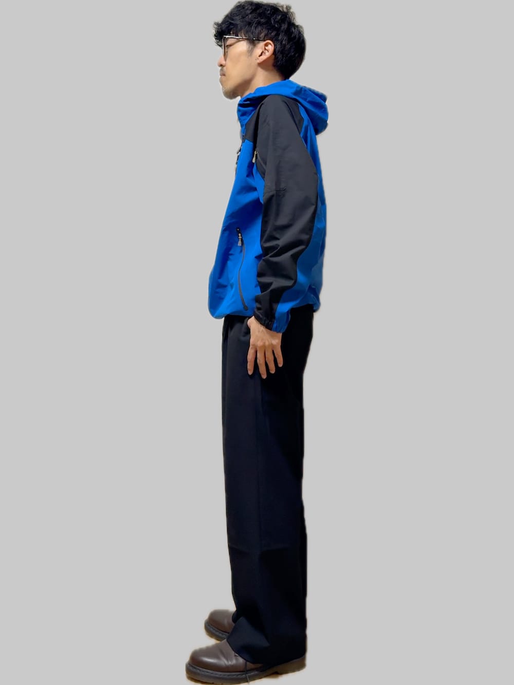 ブラウン系のドレスシューズ、ブラック系のスラックス、ブルー系のナイロンジャケットを着用したメンズの秋コーディネートの3枚目の写真