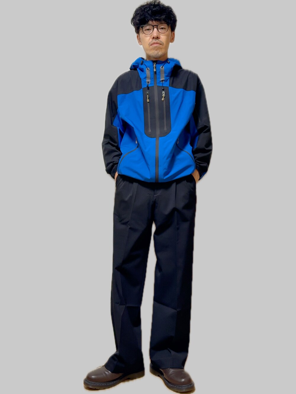 ブラウン系のドレスシューズ、ブラック系のスラックス、ブルー系のナイロンジャケットを着用したメンズの秋コーディネートの2枚目の写真