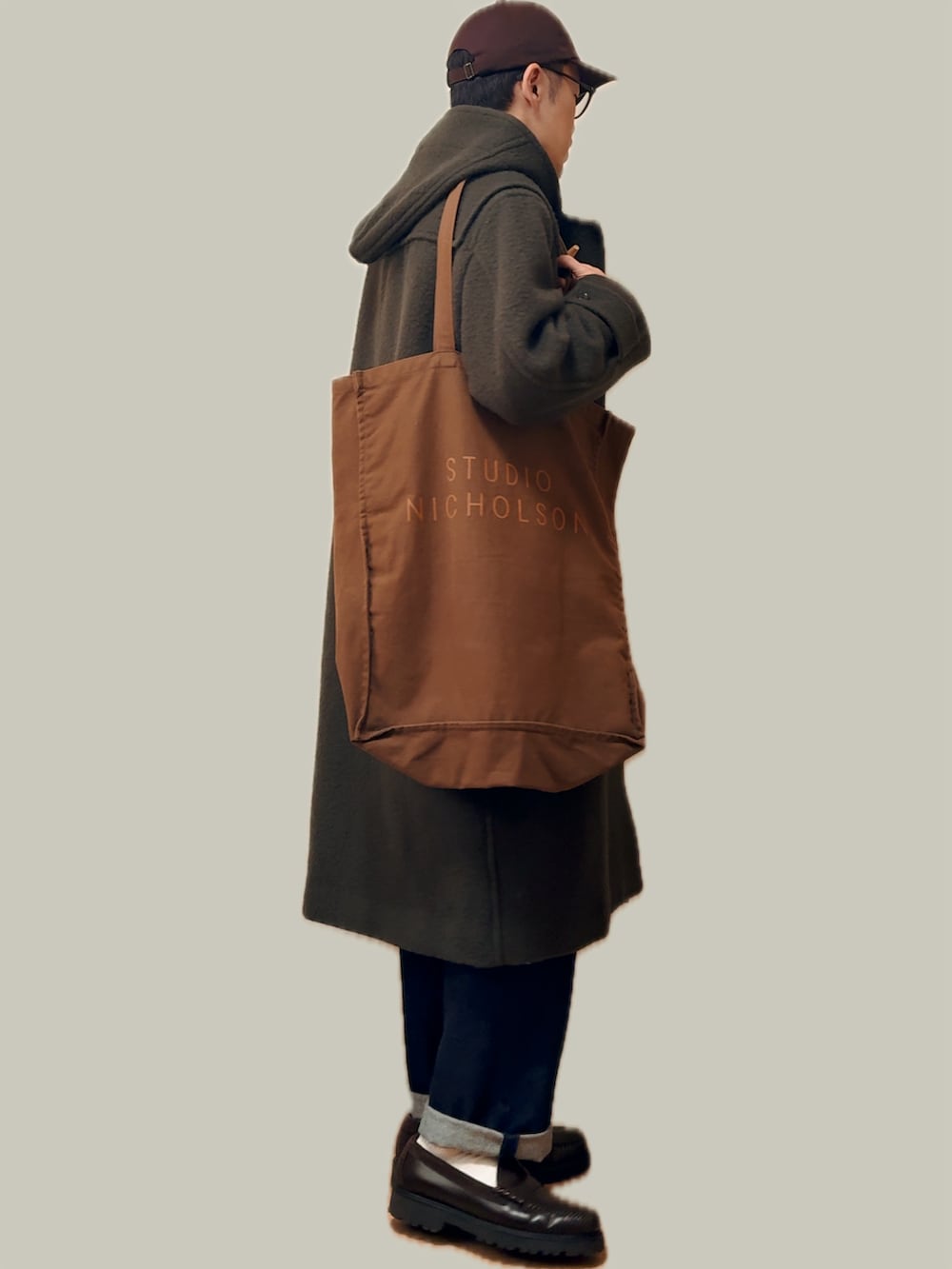 グリーン系のダッフルコート、ブラウン系のトートバッグ、ブルー系のデニムパンツを着用したメンズの冬コーディネートの3枚目の写真