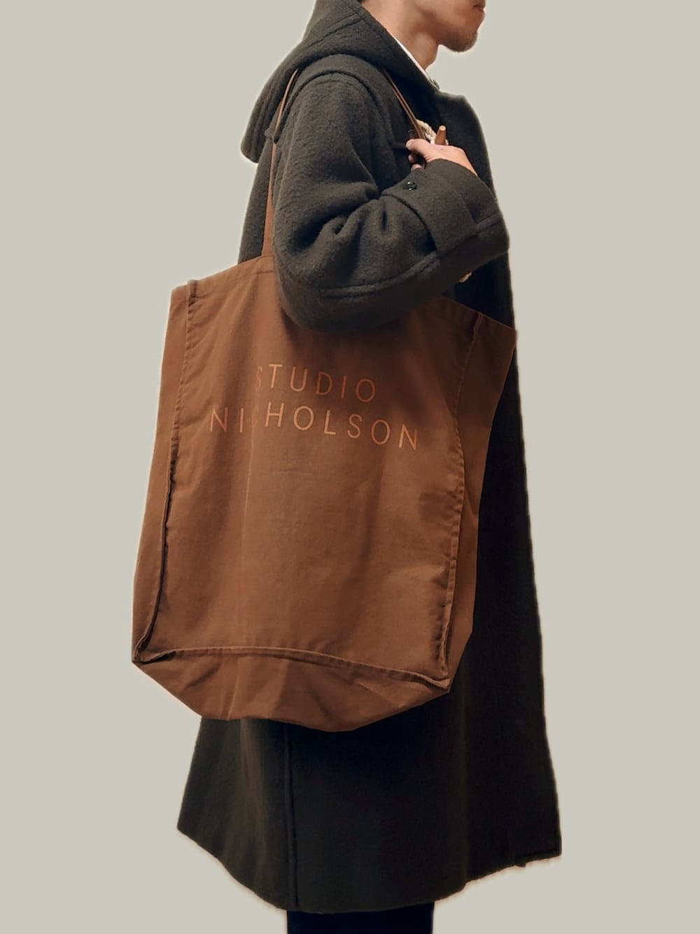 グリーン系のダッフルコート、ブラウン系のトートバッグ、ブルー系のデニムパンツを着用したメンズの冬コーディネートの4枚目の写真