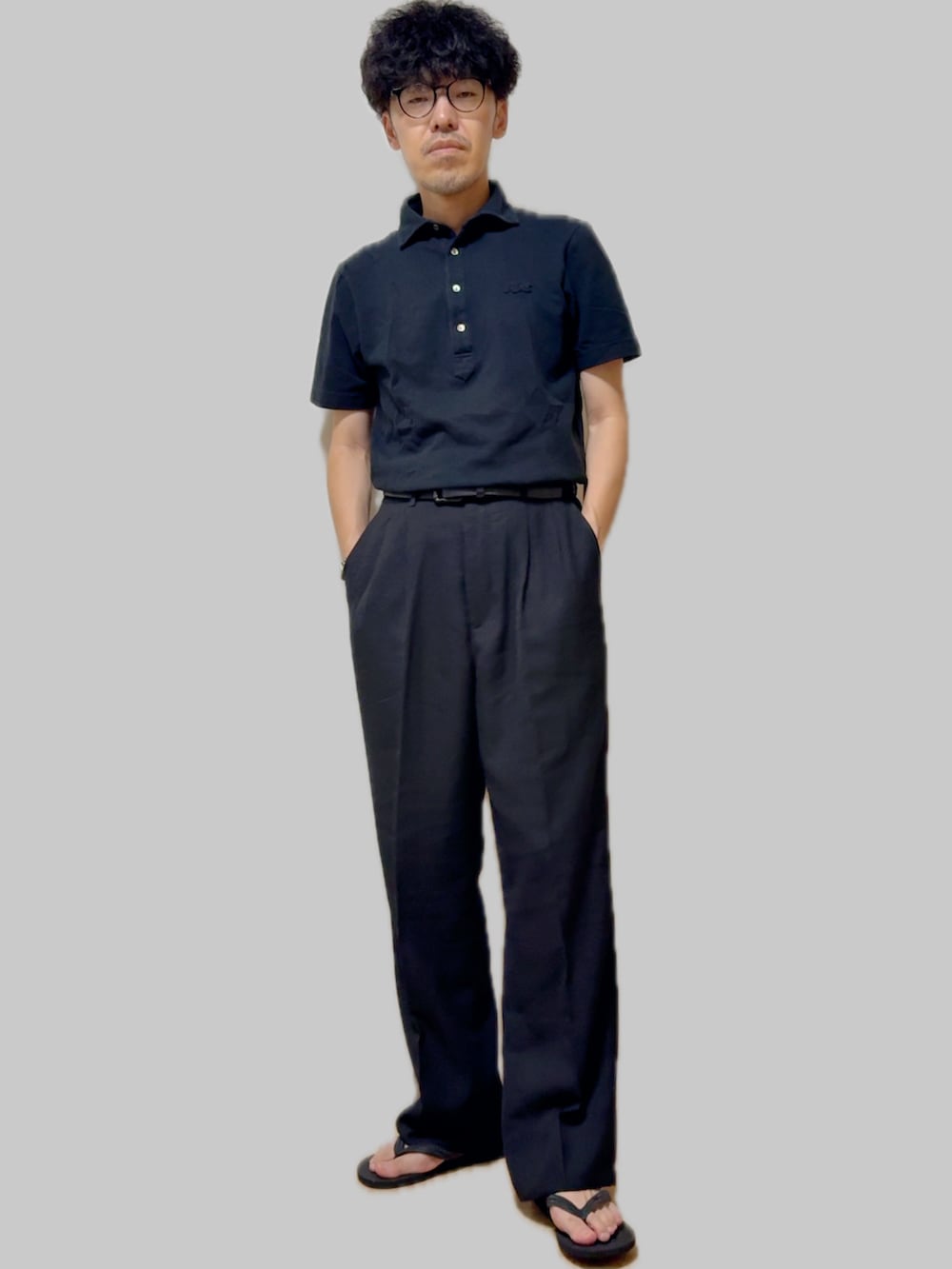 ブラック系のポロシャツ、ブラック系のスラックス、ブラック系のサンダルを着用したメンズの夏コーディネートの3枚目の写真