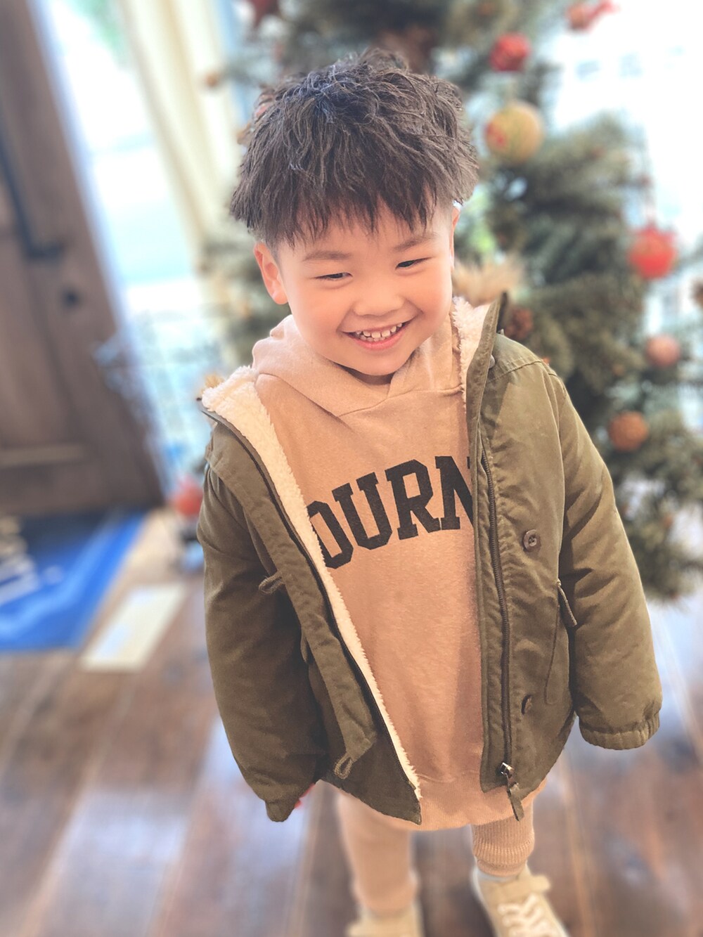 ベージュ系のパーカー、グリーン系のミリタリージャケット、ベージュ系のスラックスを着用したキッズの冬コーディネートの2枚目の写真