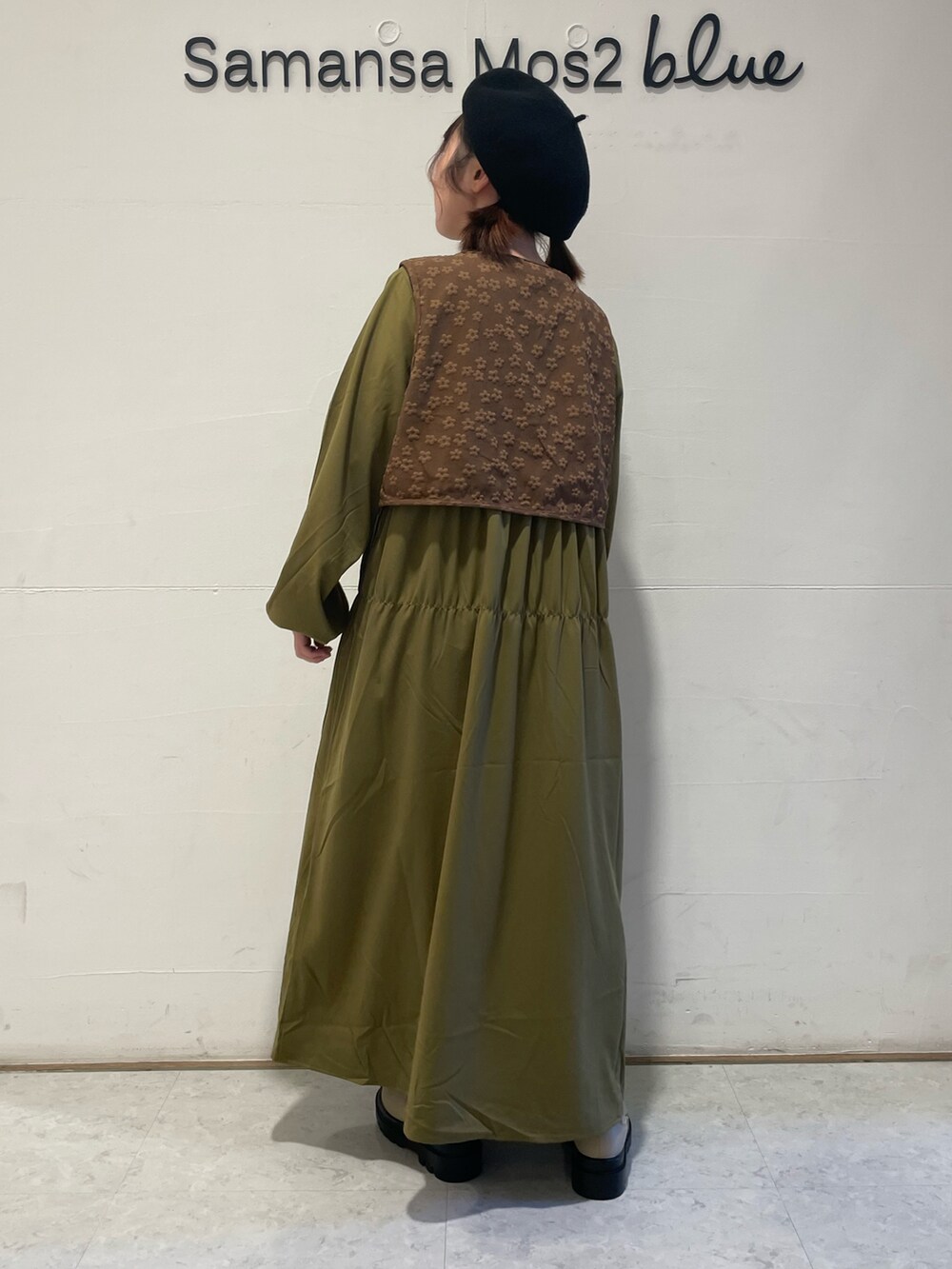 グリーン系のワンピース、ベージュ系のブーツ、ブラック系のハットを着用したレディースの秋コーディネートの2枚目の写真