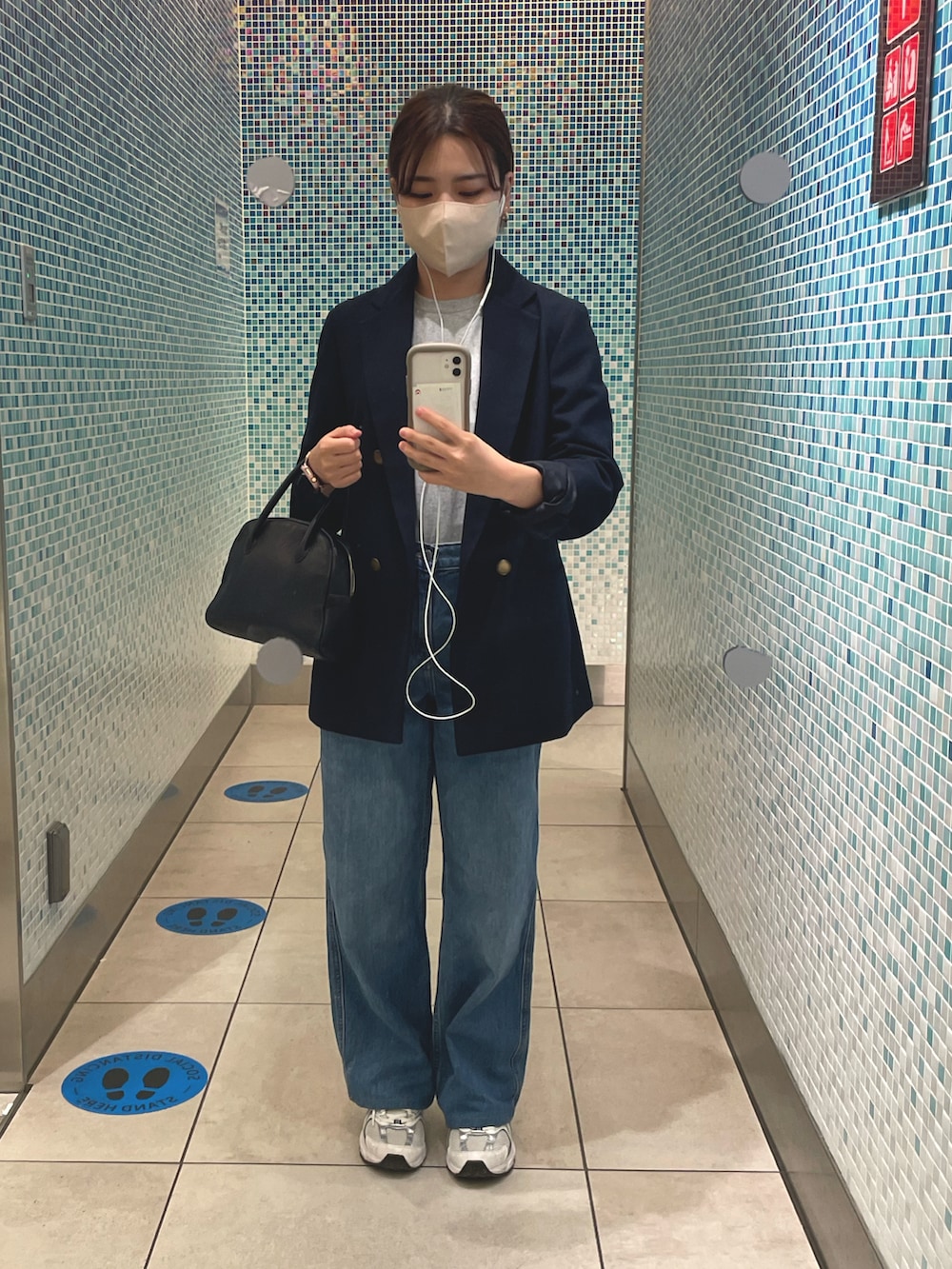 ブルー系のデニムパンツ、ホワイト系のスニーカー、ブラック系のジャケット/アウターを着用したレディースの秋コーディネートの2枚目の写真