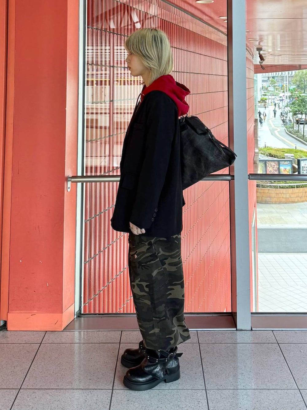 レッド系のパーカー、ブラック系のテーラードジャケット、ブラック系のブーツを着用したレディースの春コーディネートの2枚目の写真