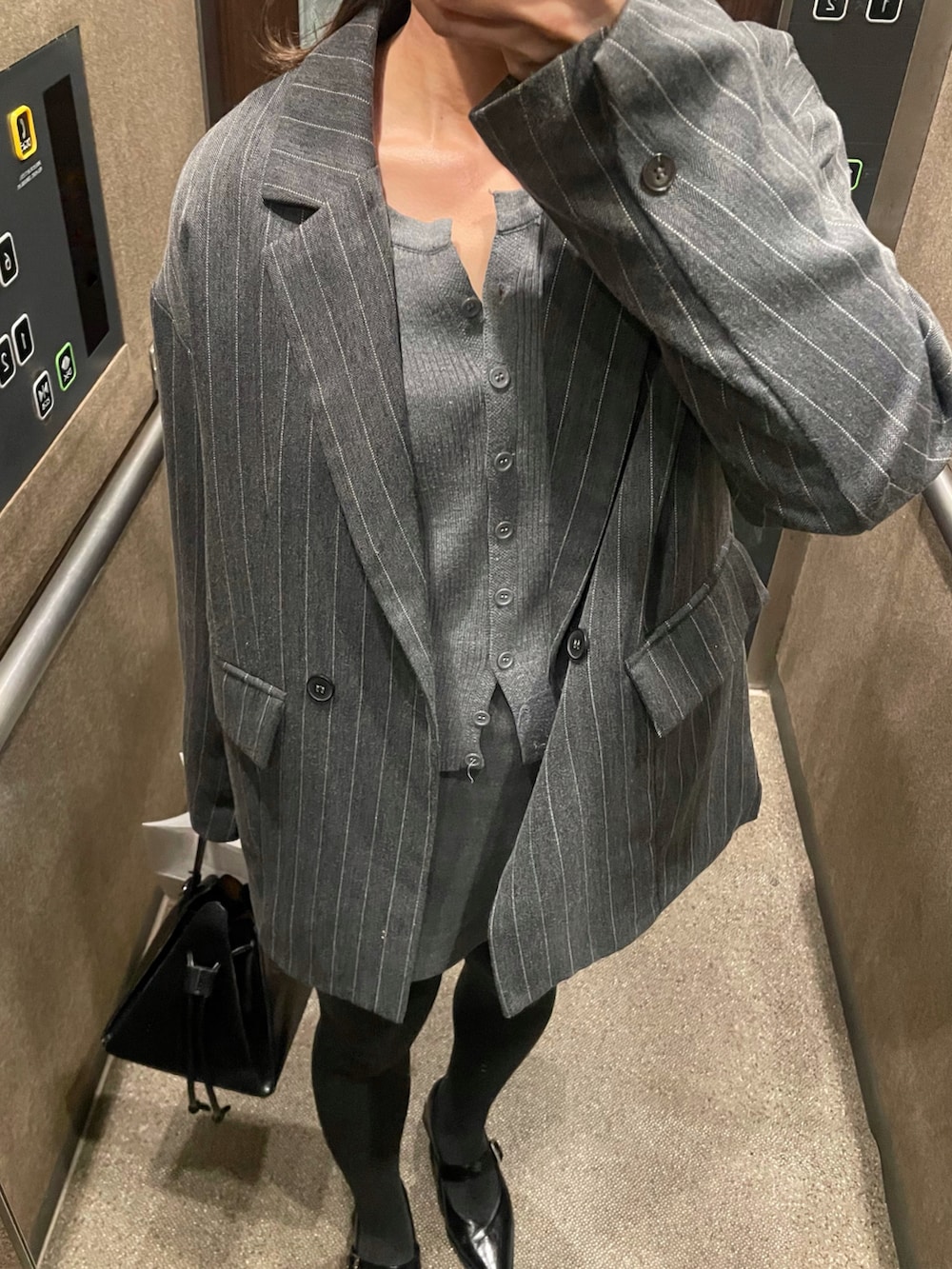 グレー系のスカート、ブラック系のハンドバッグ、グレー系のカーディガン/ボレロを着用したレディースの春コーディネートの2枚目の写真