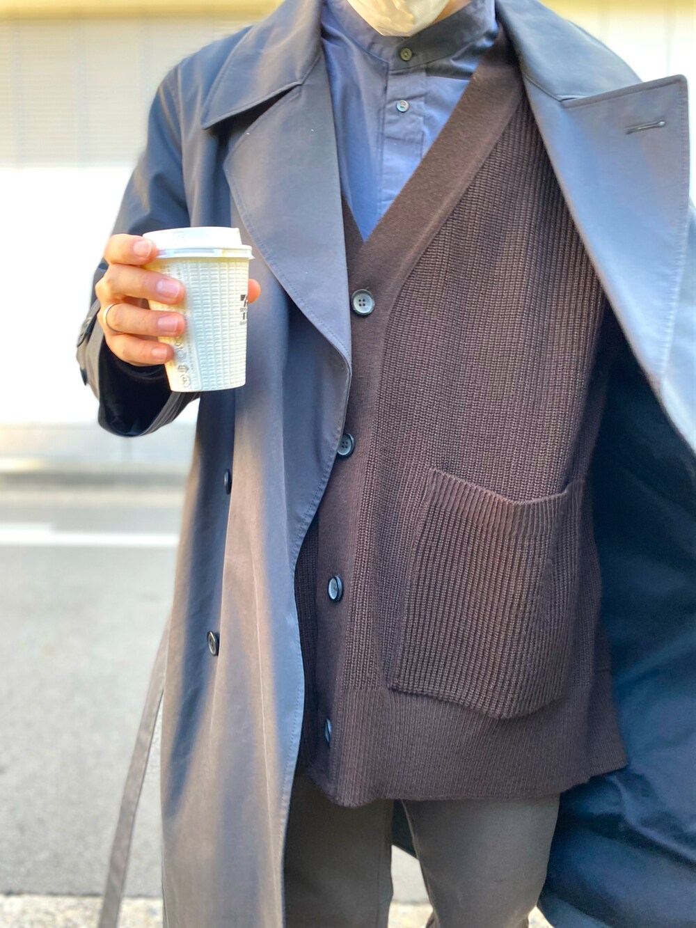 グレー系のトレンチコート、ブラック系のショルダーバッグ、ブラウン系のカーディガン/ボレロを着用したメンズの冬コーディネートの2枚目の写真