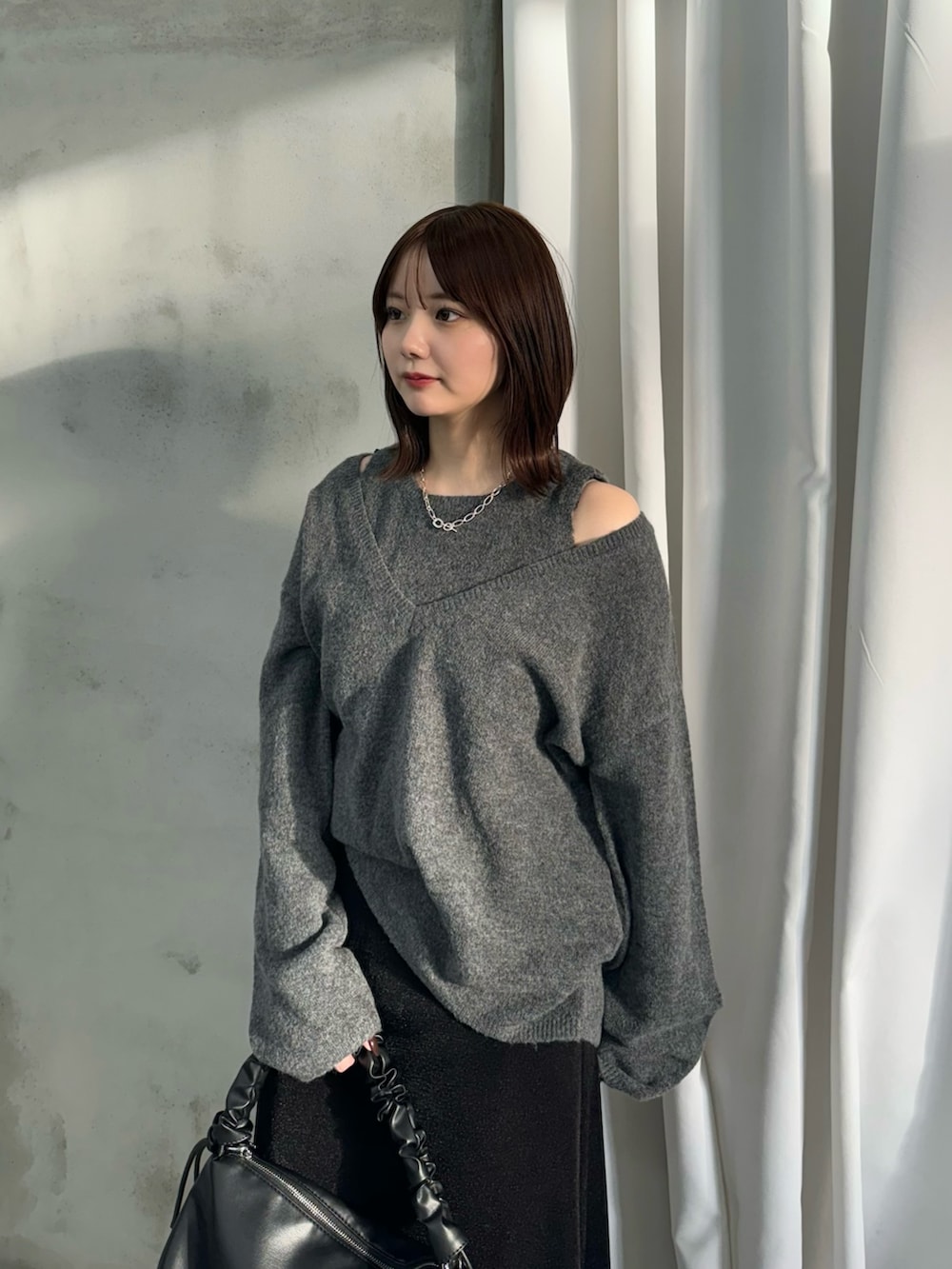 グレー系のニット/セーター、ブラック系のスカート、ブラック系のハンドバッグを着用したレディースの秋コーディネートの3枚目の写真