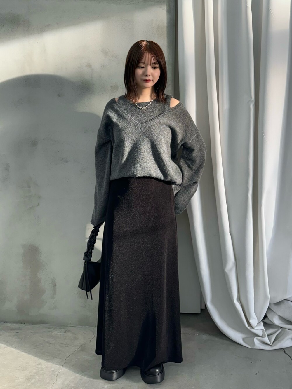 グレー系のニット/セーター、ブラック系のスカート、ブラック系のハンドバッグを着用したレディースの秋コーディネートの2枚目の写真