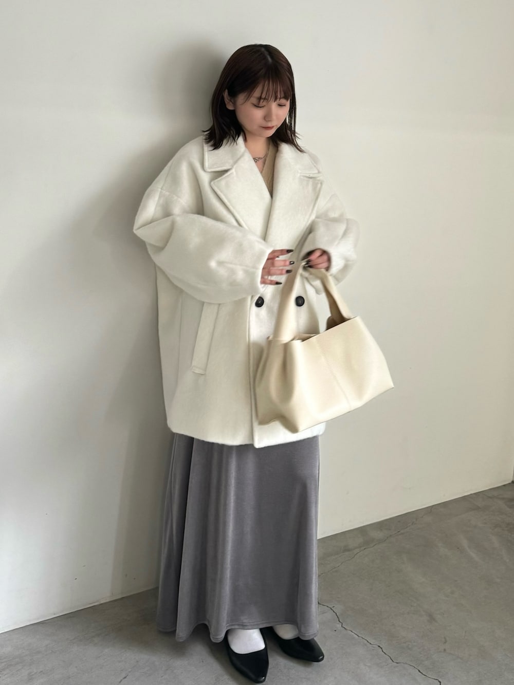 ホワイト系のチェスターコート、ベージュ系のカーディガン/ボレロ、グレー系のスカートを着用したレディースの冬コーディネートの2枚目の写真
