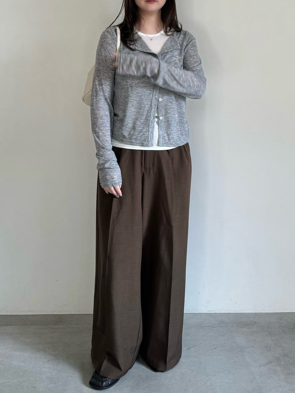 グレー系のカーディガン/ボレロ、ブラウン系のスラックス、ホワイト系のハンドバッグを着用したレディースの春コーディネートの2枚目の写真