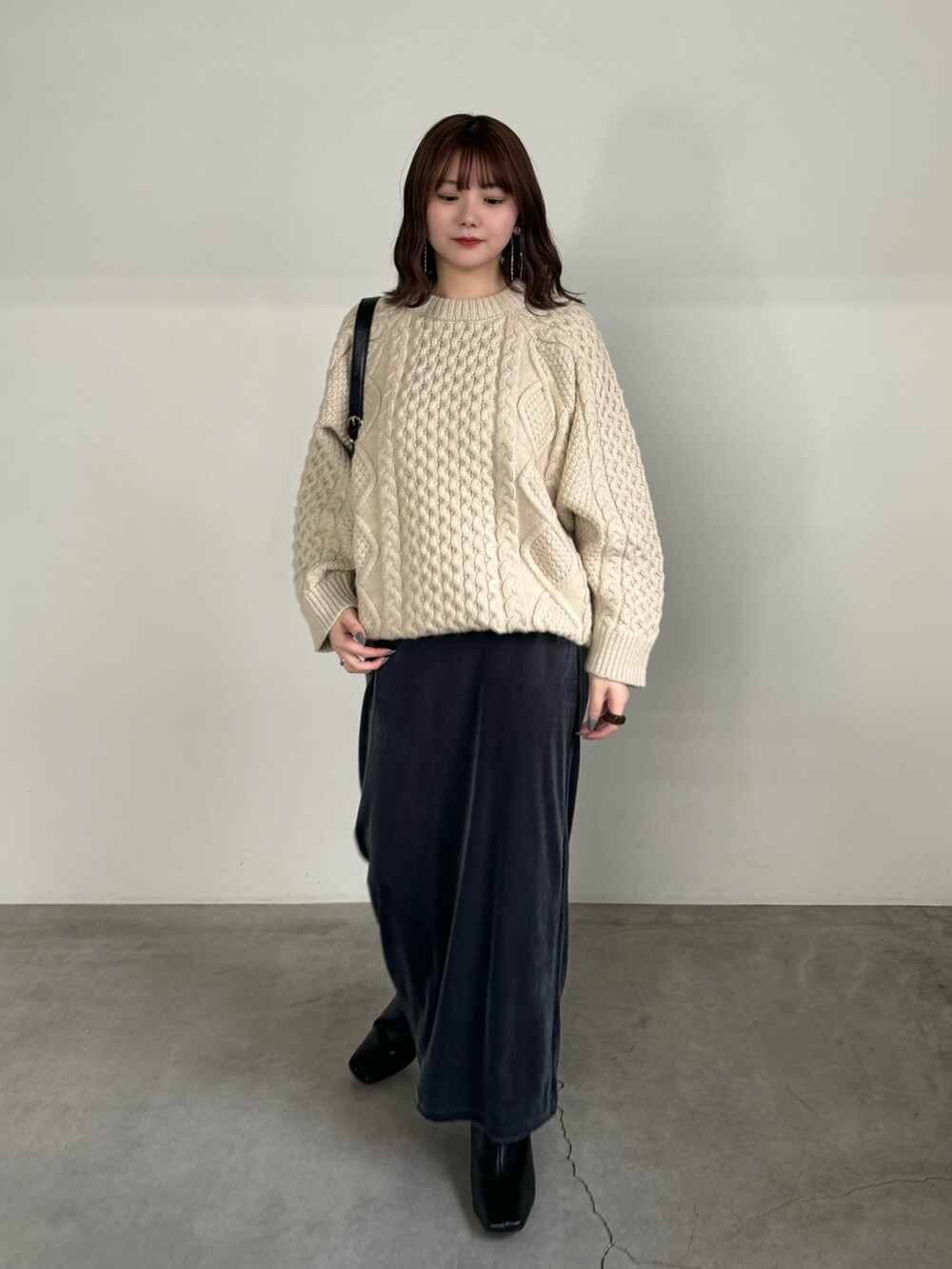 グレー系のスカート、ホワイト系のニット/セーター、ブラック系のハンドバッグを着用したレディースの秋コーディネートの2枚目の写真