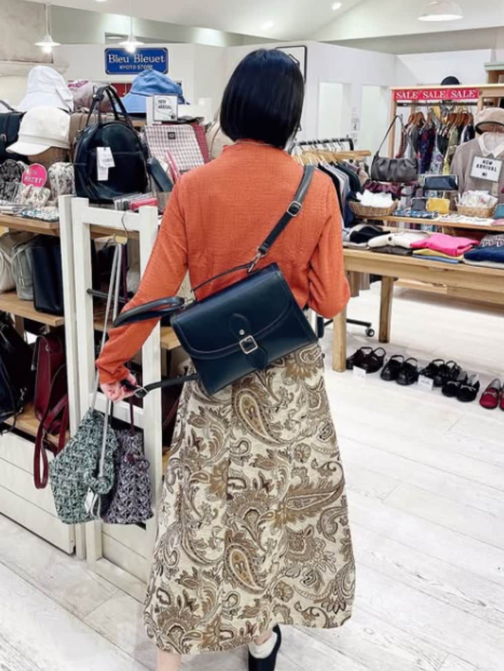 ブラック系のパンプス、オレンジ系のその他トップス、ホワイト系のスカートを着用したレディースの秋コーディネートの2枚目の写真