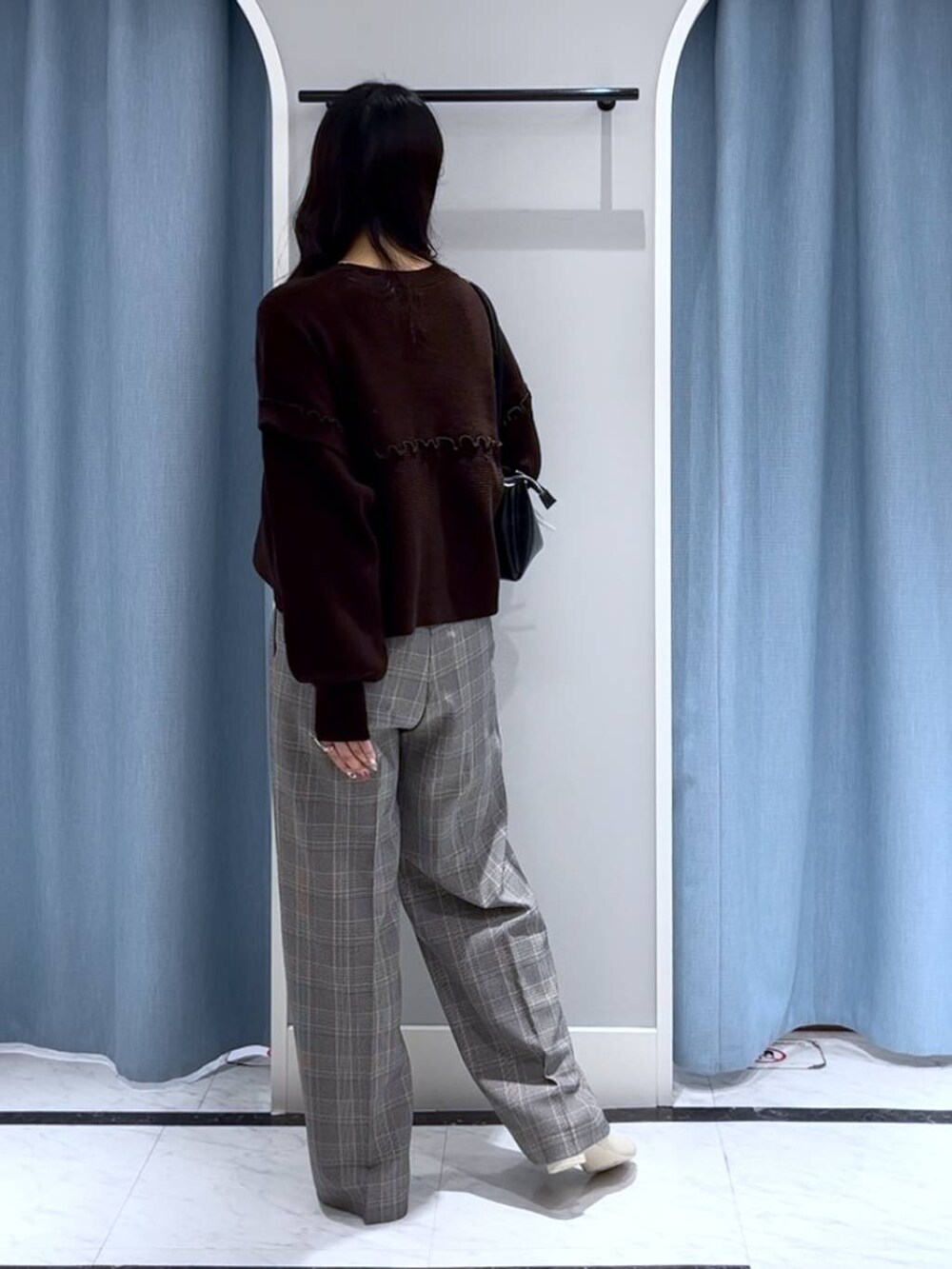 ブラック系のショルダーバッグ、ホワイト系のブーツ、グレー系のスラックスを着用したレディースの冬コーディネートの2枚目の写真