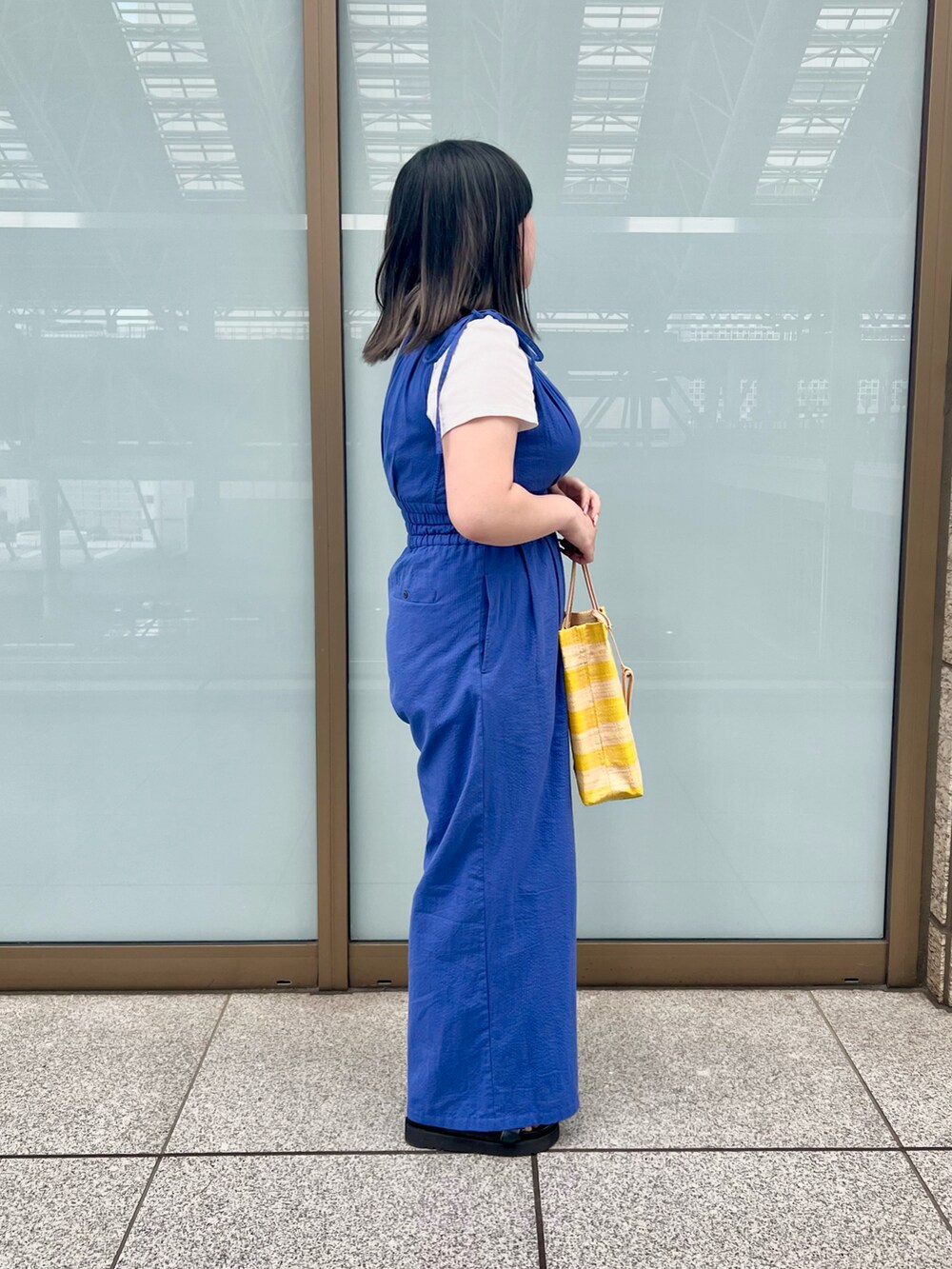 イエロー系のトートバッグ、ブルー系のサロペット/オーバーオール、ブラック系のサンダルを着用したレディースの夏コーディネートの2枚目の写真