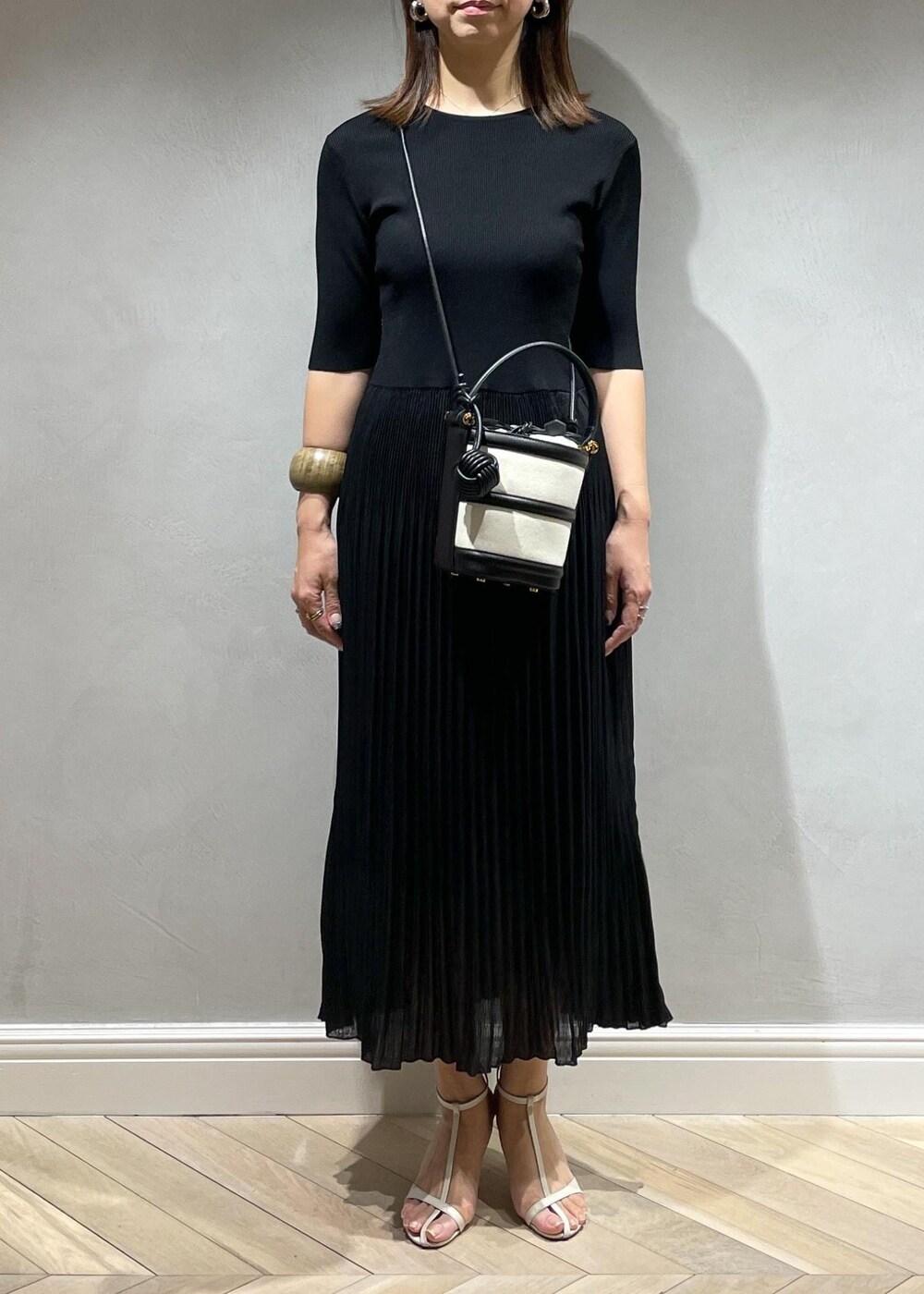 ブラック系のハンドバッグ、ホワイト系のサンダル、ブラック系のワンピースを着用したレディースの春コーディネートの5枚目の写真