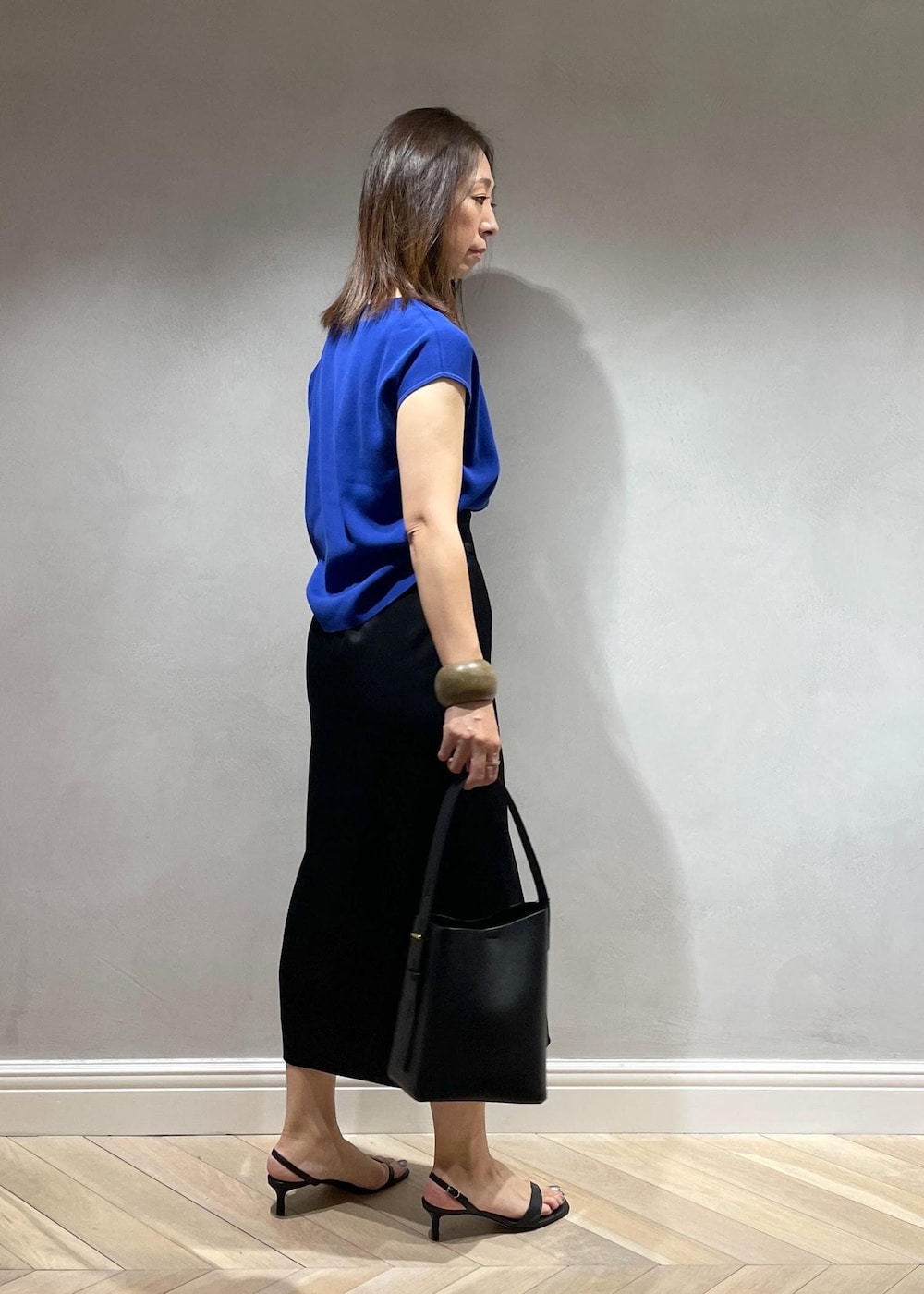 ブラック系のサンダル、ブラック系のハンドバッグ、ブルー系のニット/セーターを着用したレディースの夏コーディネートの3枚目の写真