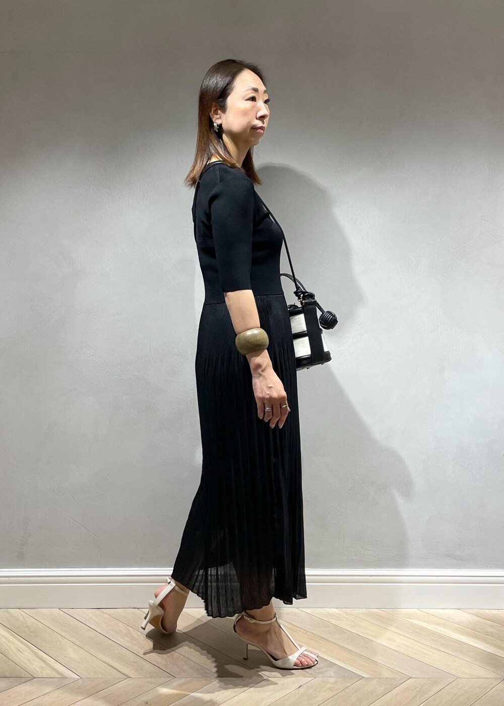 ブラック系のハンドバッグ、ホワイト系のサンダル、ブラック系のワンピースを着用したレディースの春コーディネートの3枚目の写真