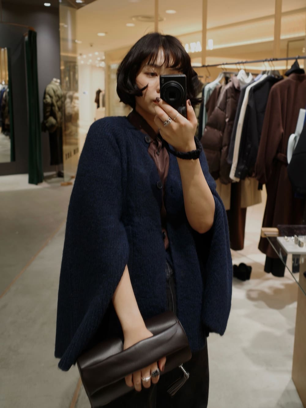 ブラック系のデニムパンツ、ブルー系のカーディガン/ボレロ、ブラウン系のクラッチバッグを着用したレディースの秋コーディネートの2枚目の写真