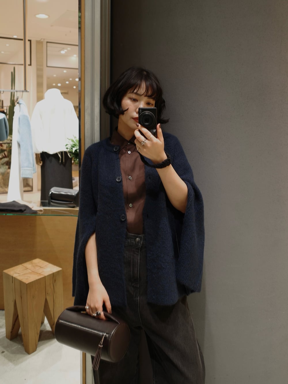 ブラック系のデニムパンツ、ブルー系のカーディガン/ボレロ、ブラウン系のクラッチバッグを着用したレディースの秋コーディネートの3枚目の写真