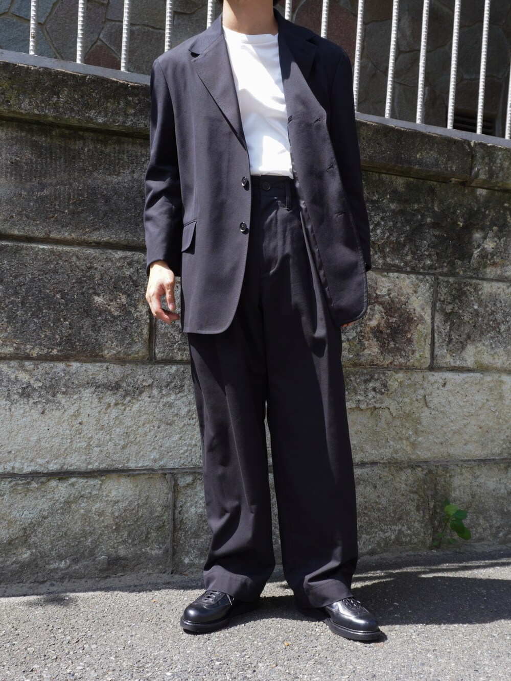 ホワイト系のTシャツ/カットソー、ブラック系のテーラードジャケット、ブラック系のスラックスを着用したメンズの夏コーディネートの2枚目の写真