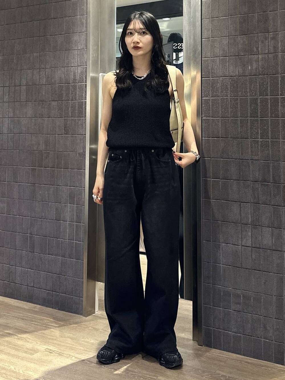 ブラック系のデニムパンツ、ホワイト系のショルダーバッグ、ブラック系のタンクトップを着用したレディースの夏コーディネートの3枚目の写真