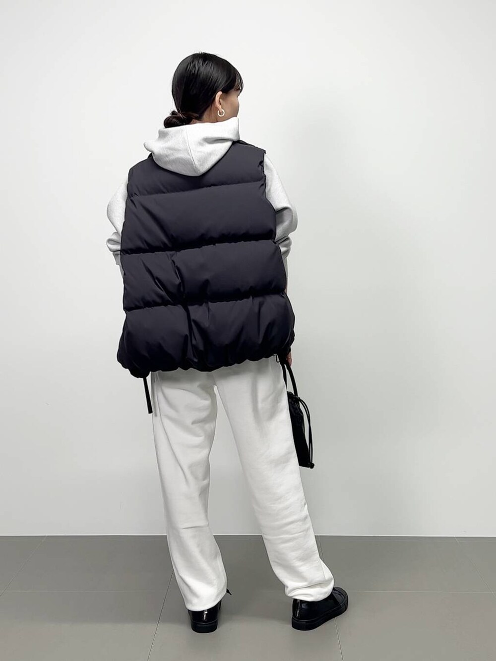 ブラック系のショルダーバッグ、ブラック系のダウンベスト、ホワイト系のスニーカーを着用したレディースの秋コーディネートの3枚目の写真