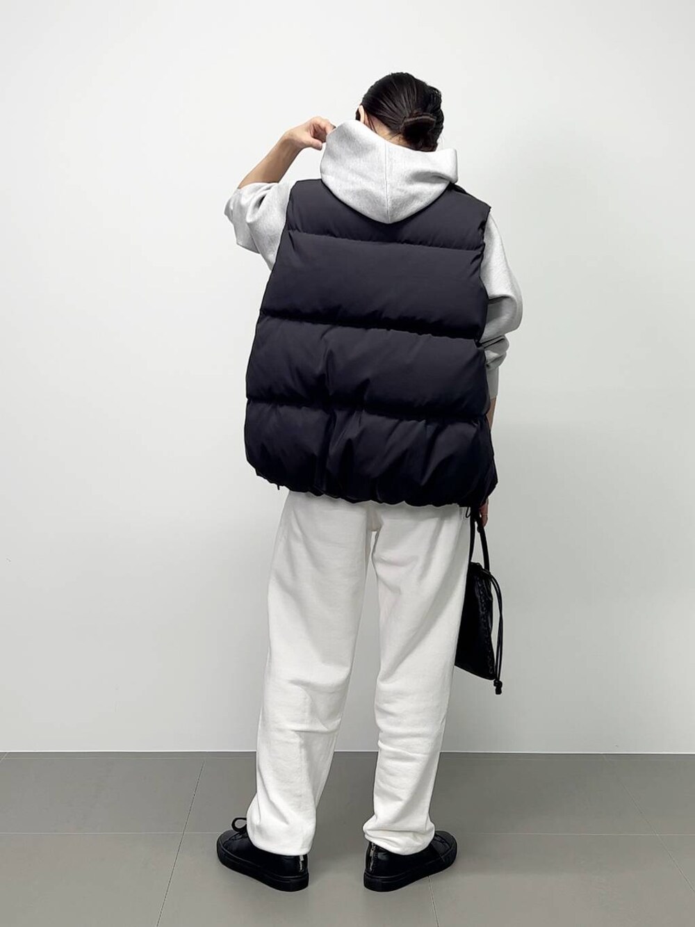 ブラック系のショルダーバッグ、ブラック系のダウンベスト、ホワイト系のスニーカーを着用したレディースの秋コーディネートの4枚目の写真