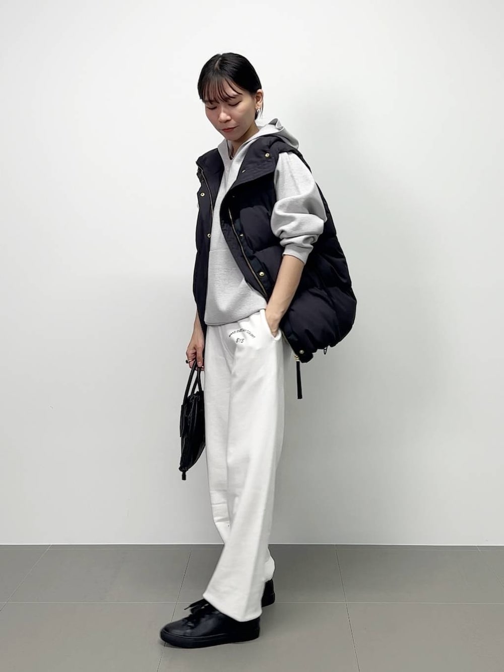 ブラック系のショルダーバッグ、ブラック系のダウンベスト、ホワイト系のスニーカーを着用したレディースの秋コーディネートの2枚目の写真