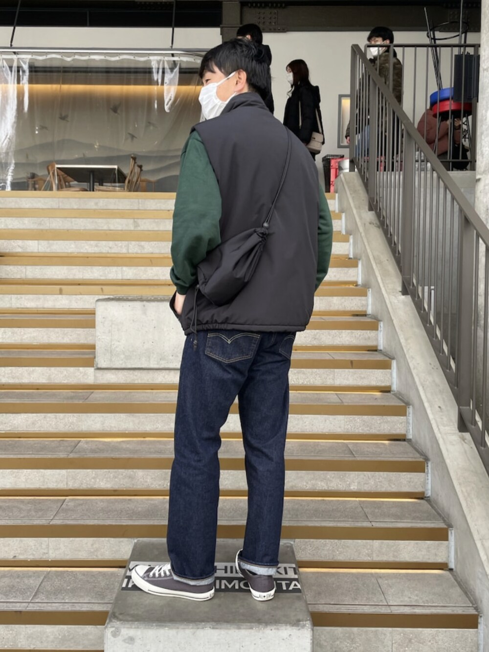 ブルー系のデニムパンツ、ホワイト系のスニーカー、ブラック系のダウンベストを着用したメンズの春コーディネートの2枚目の写真