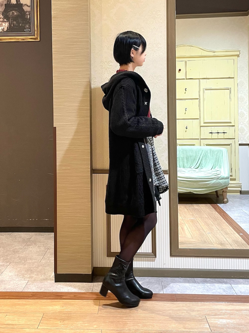 レッド系のニット/セーター、ブラック系のその他アウター、ブラック系のブーツを着用したレディースの秋コーディネートの2枚目の写真