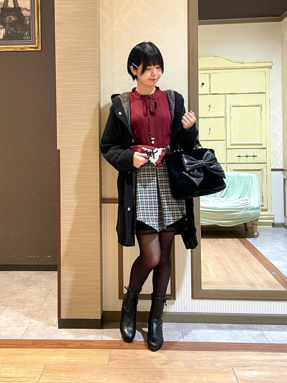 レッド系のニット/セーター、ブラック系のその他アウター、ブラック系のブーツを着用したレディースの秋コーディネートの4枚目の写真