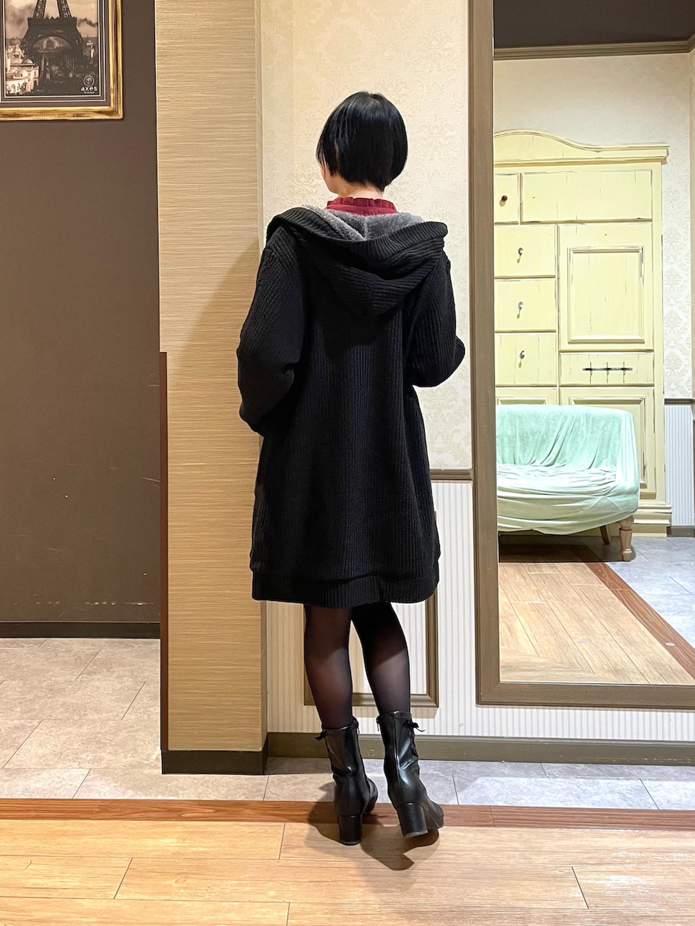 レッド系のニット/セーター、ブラック系のその他アウター、ブラック系のブーツを着用したレディースの秋コーディネートの3枚目の写真