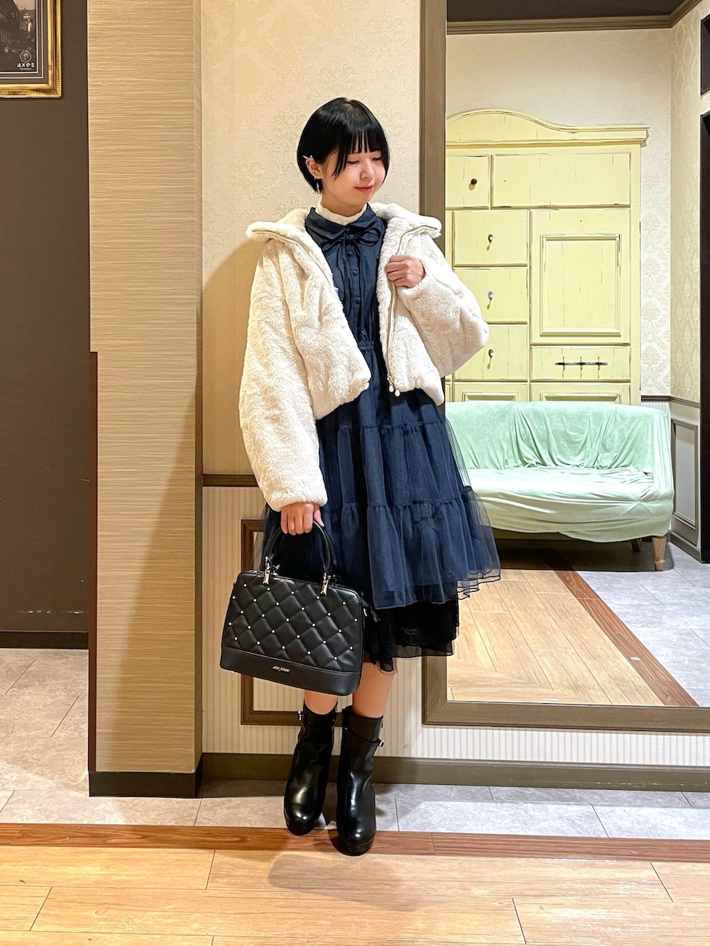 ホワイト系のピーコート、ブルー系のワンピース、ブラック系のブーツを着用したレディースの秋コーディネートの2枚目の写真