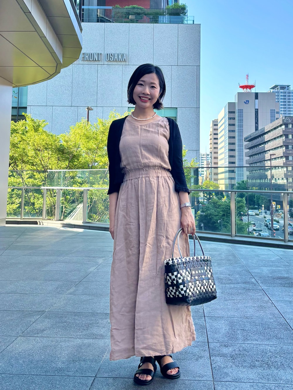 ベージュ系のワンピース、ブラック系のカーディガン/ボレロ、ブラック系のかごバッグを着用したレディースの夏コーディネートの2枚目の写真