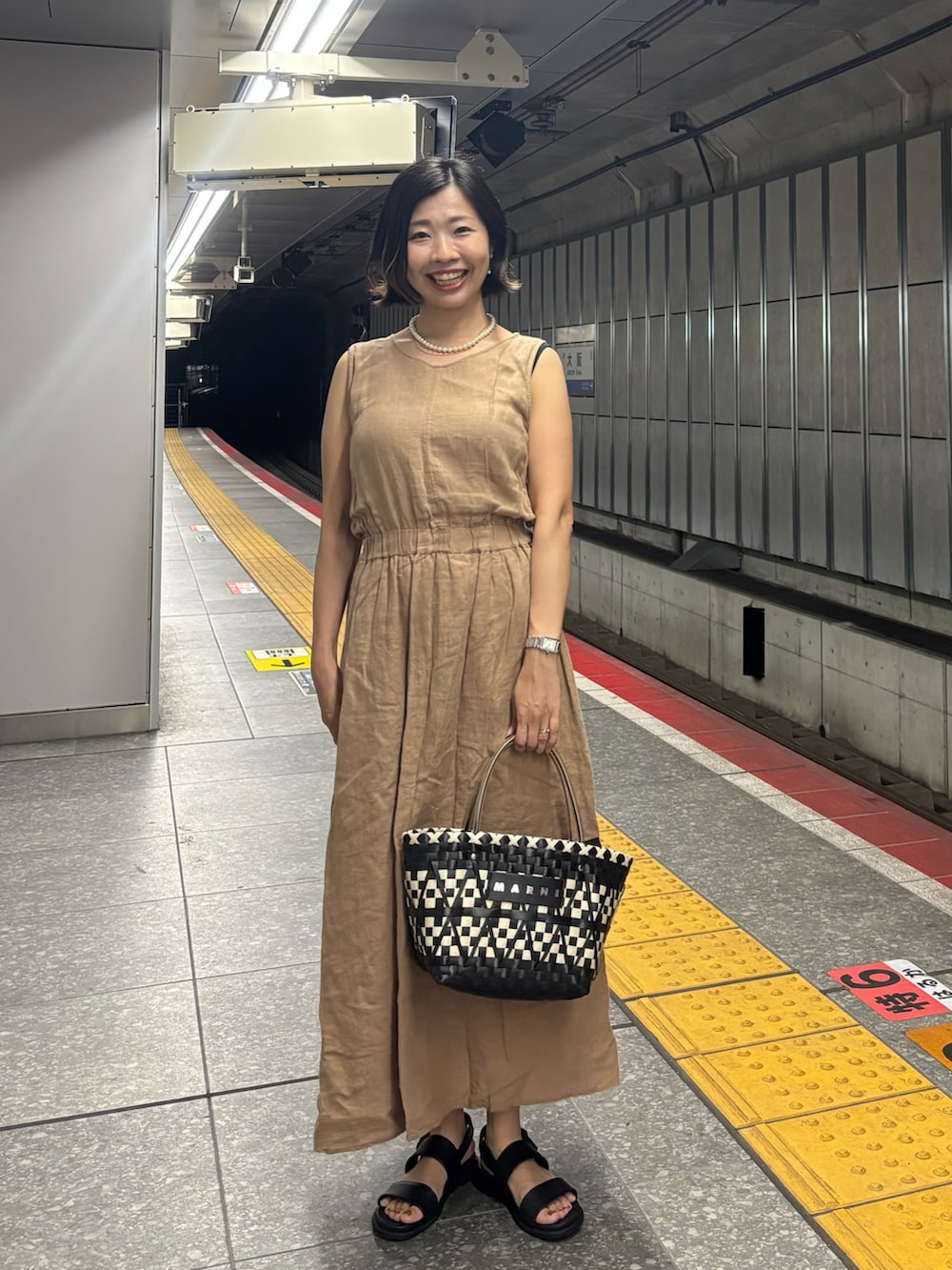 ベージュ系のワンピース、ブラック系のカーディガン/ボレロ、ブラック系のかごバッグを着用したレディースの夏コーディネートの3枚目の写真