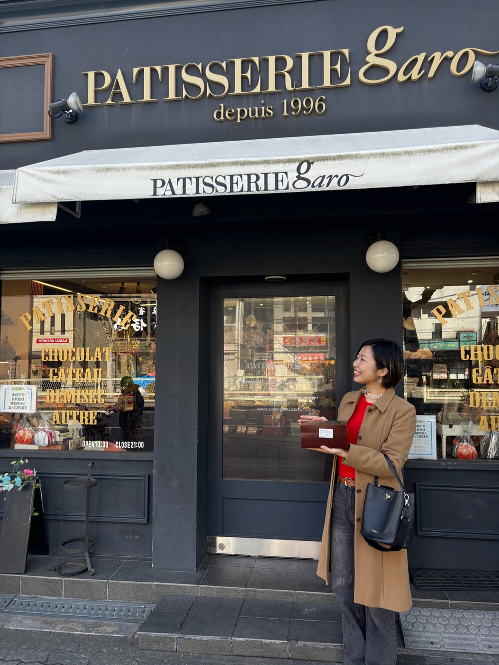 ブラウン系のステンカラーコート、レッド系のニット/セーター、グレー系のデニムパンツを着用したレディースの冬コーディネートの2枚目の写真