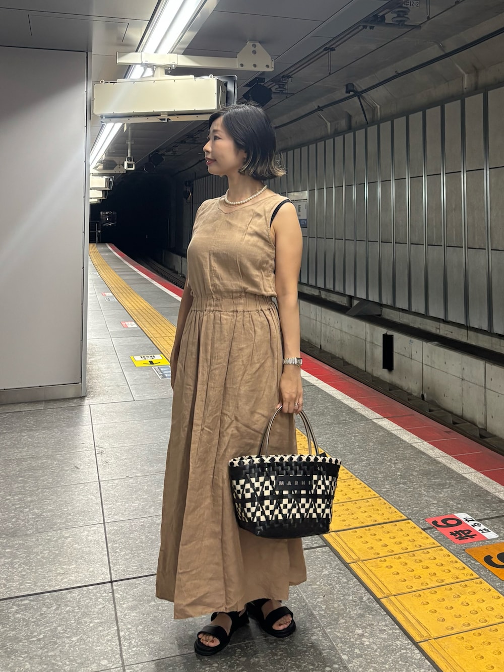 ベージュ系のワンピース、ブラック系のカーディガン/ボレロ、ブラック系のかごバッグを着用したレディースの夏コーディネートの4枚目の写真
