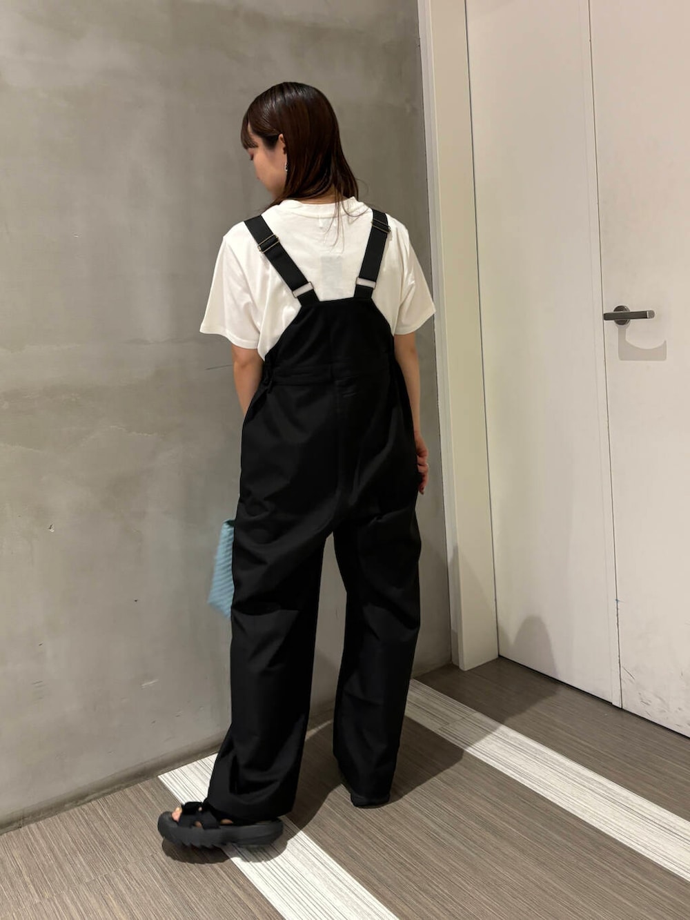 ブルー系のトートバッグ、ブラック系のサロペット/オーバーオール、ホワイト系のTシャツ/カットソーを着用したレディースの夏コーディネートの3枚目の写真