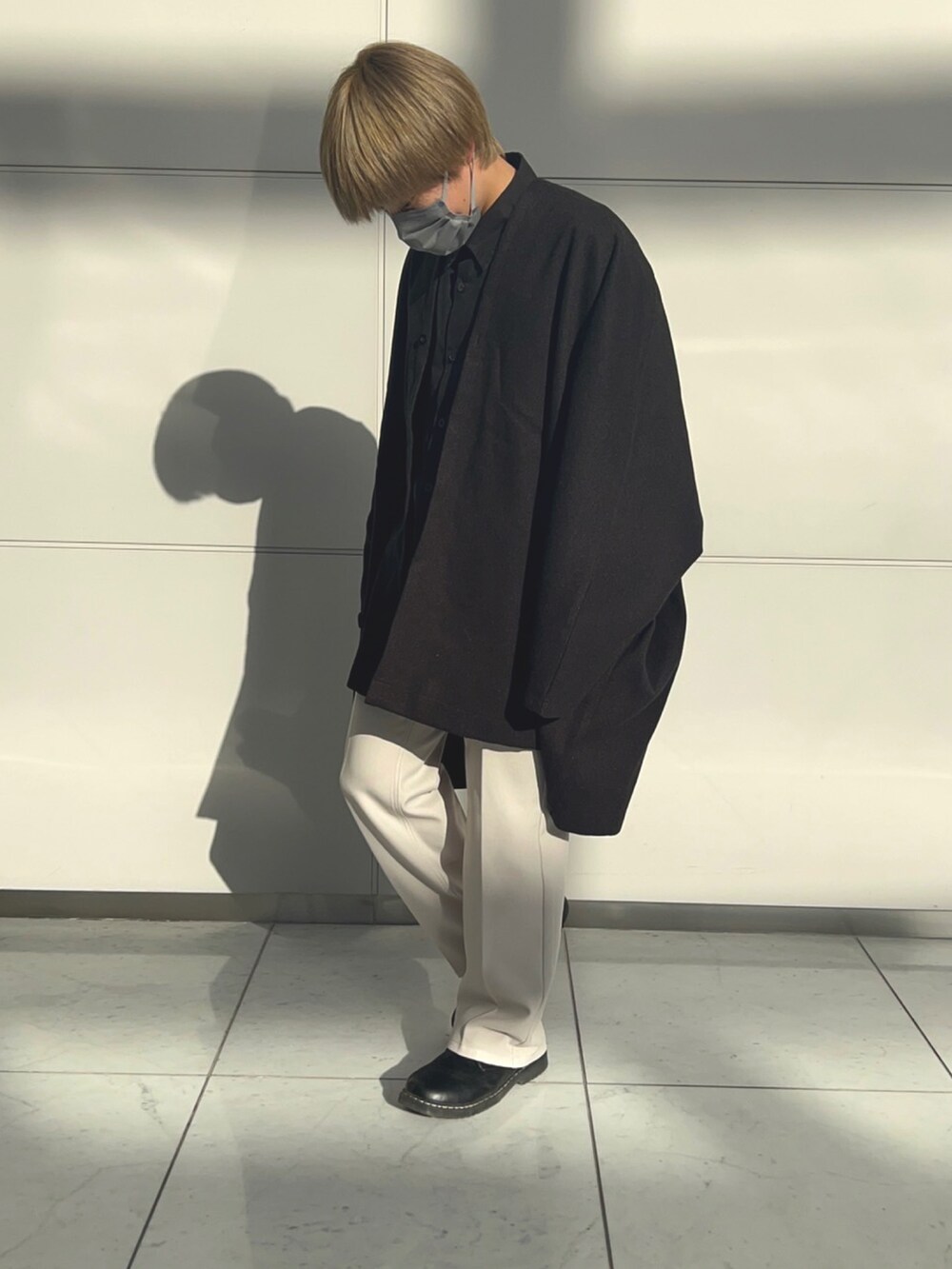 ブラック系のポンチョ、ブラック系のドレスシューズ、ホワイト系のパンツを着用したメンズの春コーディネートの2枚目の写真