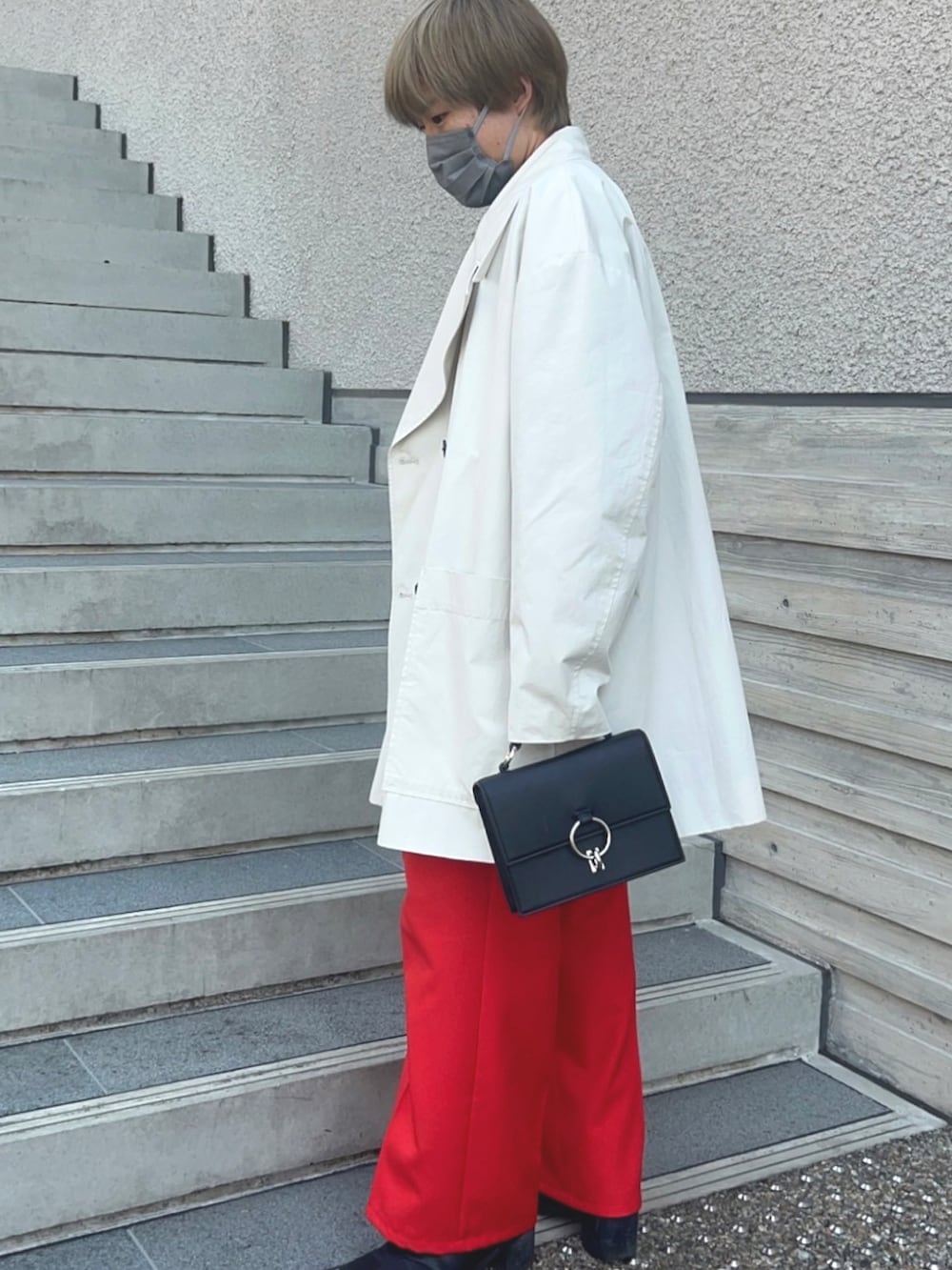 ベージュ系のステンカラーコート、レッド系のスラックス、ブラック系のブーツを着用したメンズの春コーディネートの2枚目の写真