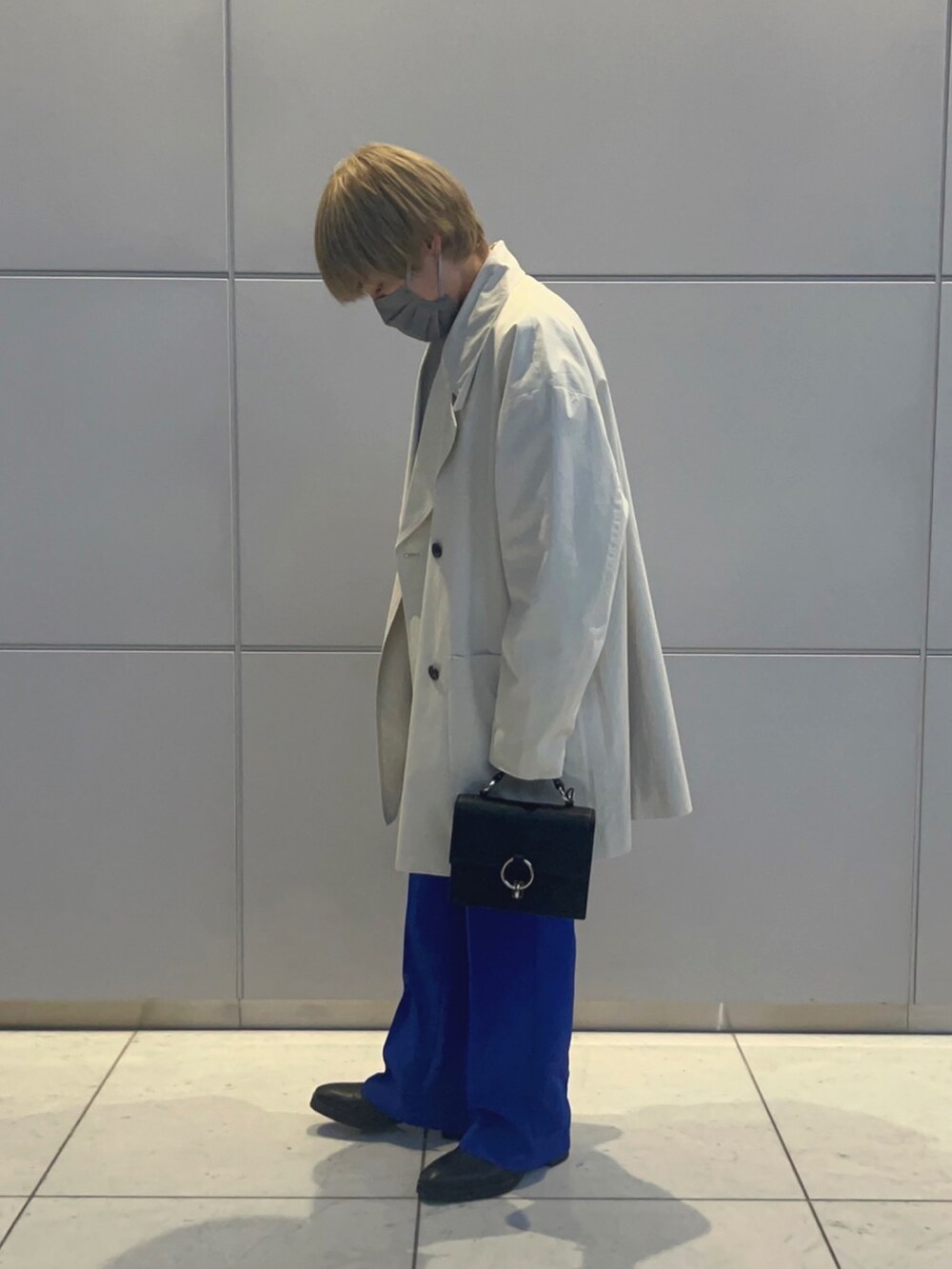 ベージュ系のステンカラーコート、ブラック系のショルダーバッグ、ブラック系のブーツを着用したメンズの春コーディネートの3枚目の写真