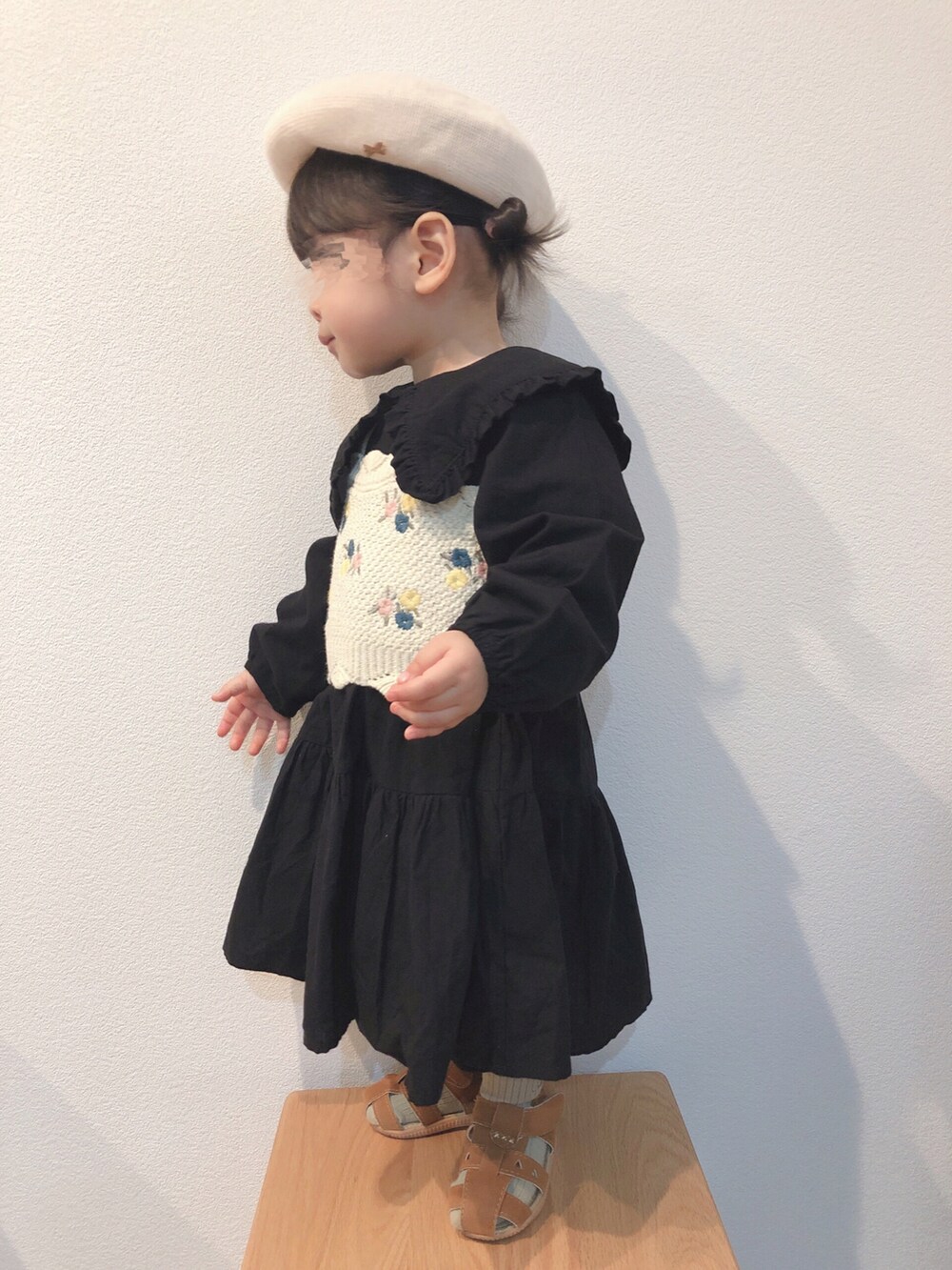 ブラック系のワンピース、ベージュ系のニット/セーター、ブラウン系のサンダルを着用したキッズの春コーディネートの2枚目の写真